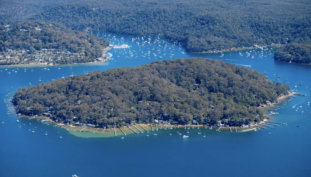 Screenshot 2025-05-06 at 8.42.21 AM Aerial image of Scotland Island surrounded by calm Pittwater waters, moored boats, and private jetties nestled among the trees